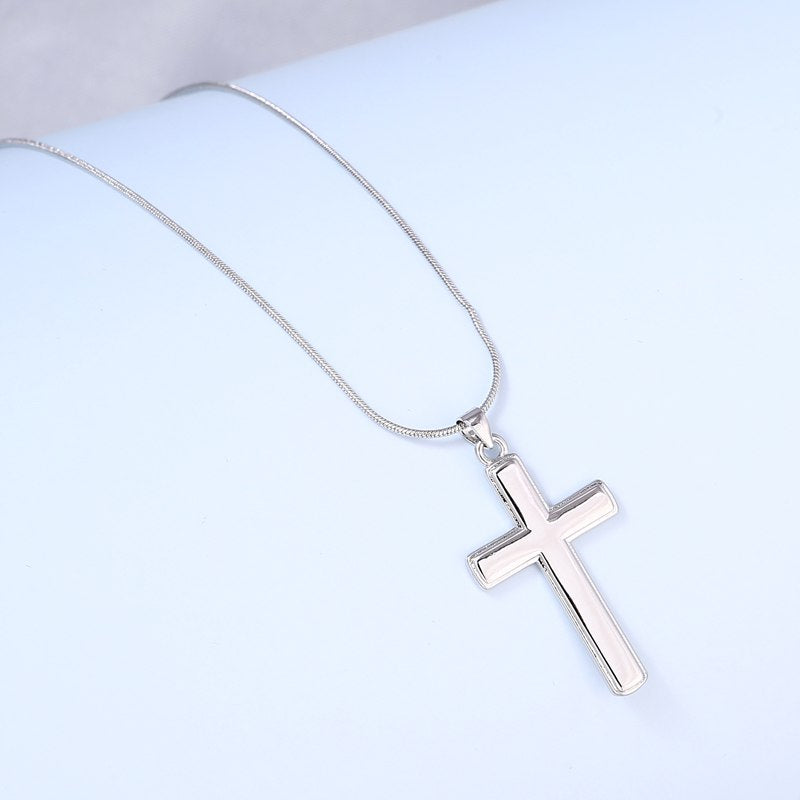 Silver cross pendant on snake chain necklace laid on light blue surface, close-up