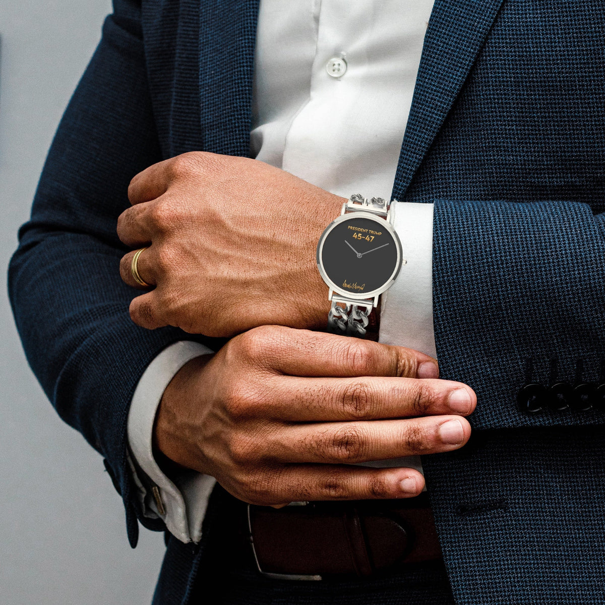 Man in navy suit wearing the President Trump 45-47 watch with silver chain-link strap