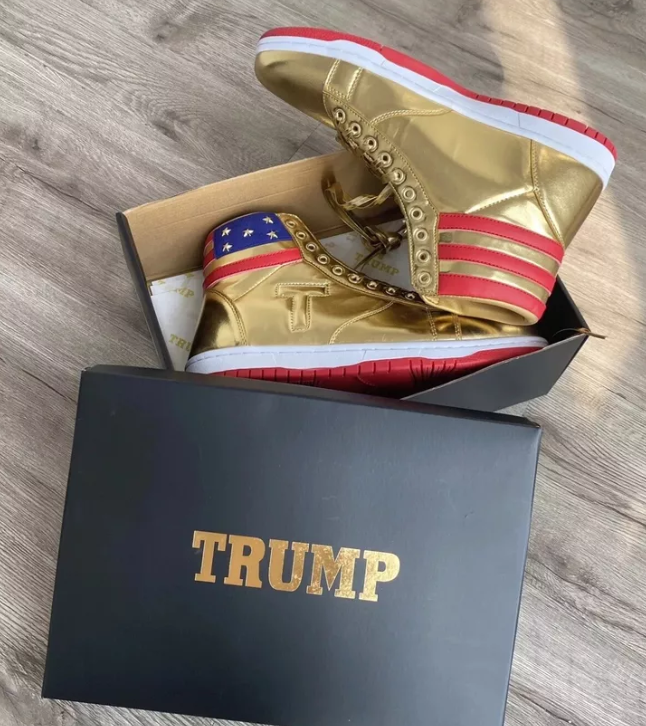 Gold Trump Never Surrender high-top sneakers in open box beside black TRUMP-branded lid