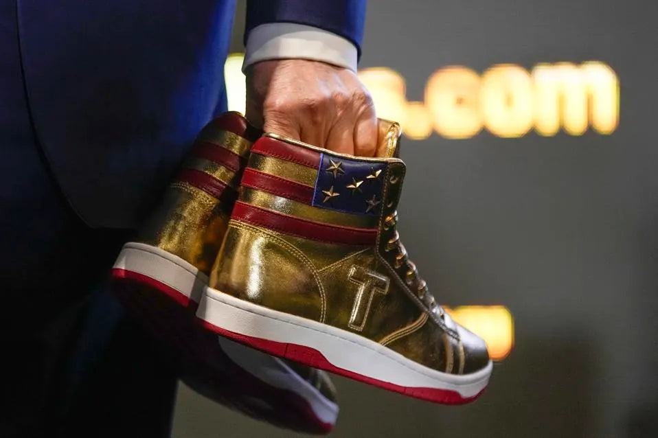 Gold Trump Never Surrender high-top sneakers held in hand at a trumpsneakers.com event