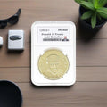 Donald J. Trump 2025 gold medallion in slab case on wooden desk