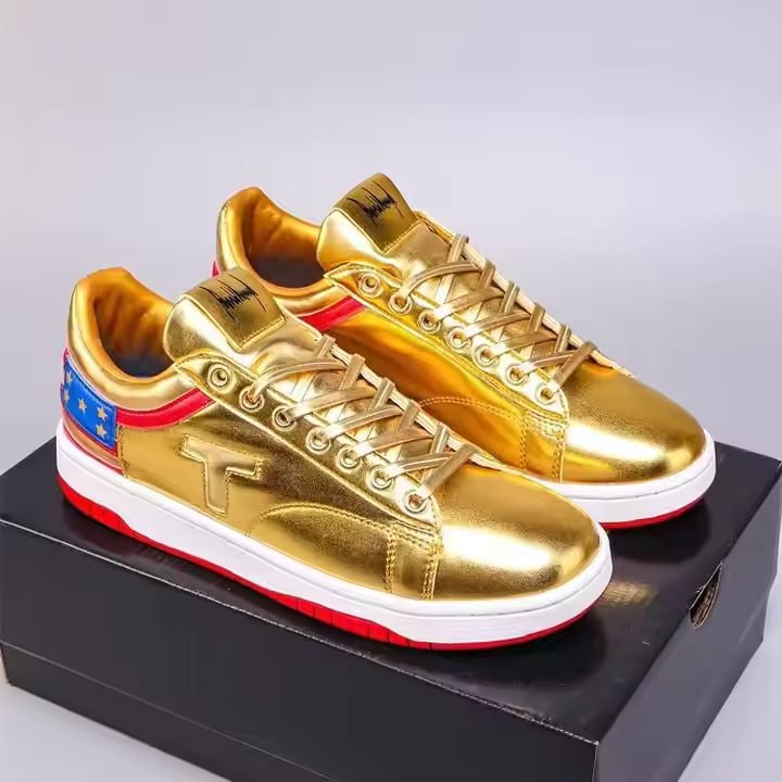 Pair of Never Surrender gold low top sneakers with red and star heel, resting on box